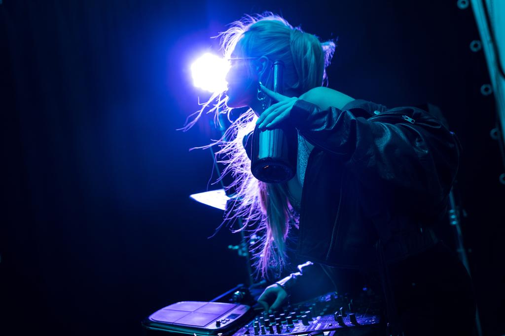 blonde stylish dj girl touching dj equipment while holding bottle in nightclub  - Photo, Image