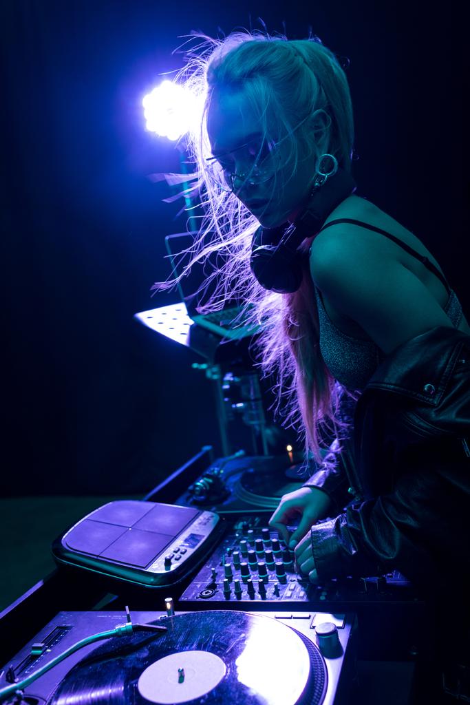 κομψό dj κορίτσι αγγίζει εξοπλισμός dj ενώ στέκεται σε νυχτερινό κέντρο διασκέδασης  - Φωτογραφία, εικόνα