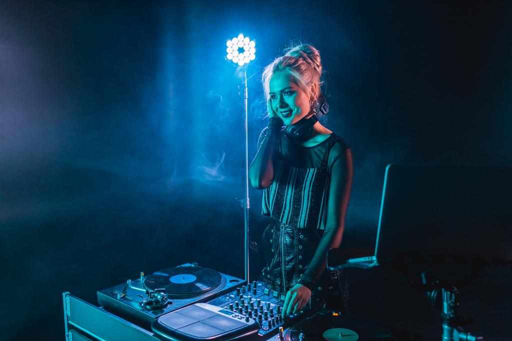 счастливая блондинка в наушниках, стоящая рядом с диджеем в ночном клубе с дымом
  - Фото, изображение