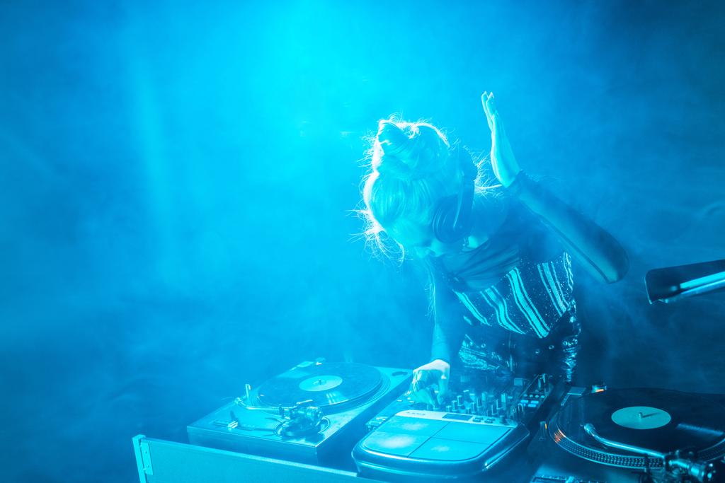 blond dj dívka poslech hudby ve sluchátkách při používání dj vybavení v nočním klubu s kouřem  - Fotografie, Obrázek