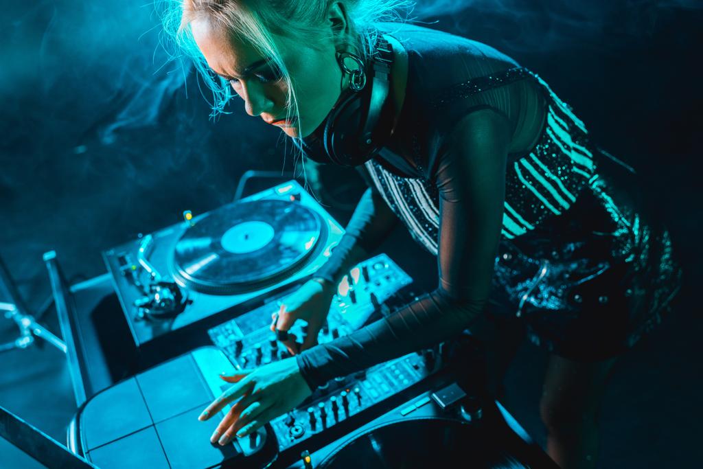 enfocado hermosa chica dj usando dj equipo en discoteca con humo
  - Foto, imagen