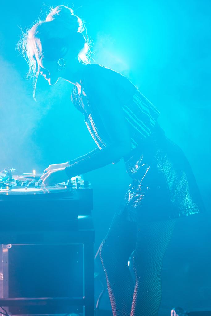beautiful dj woman with blonde hair using dj mixer in nightclub with smoke - Photo, Image