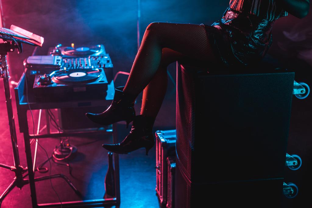Обрезанный вид женщины-диджея, сидящей возле диджейского оборудования в ночном клубе с дымом
  - Фото, изображение