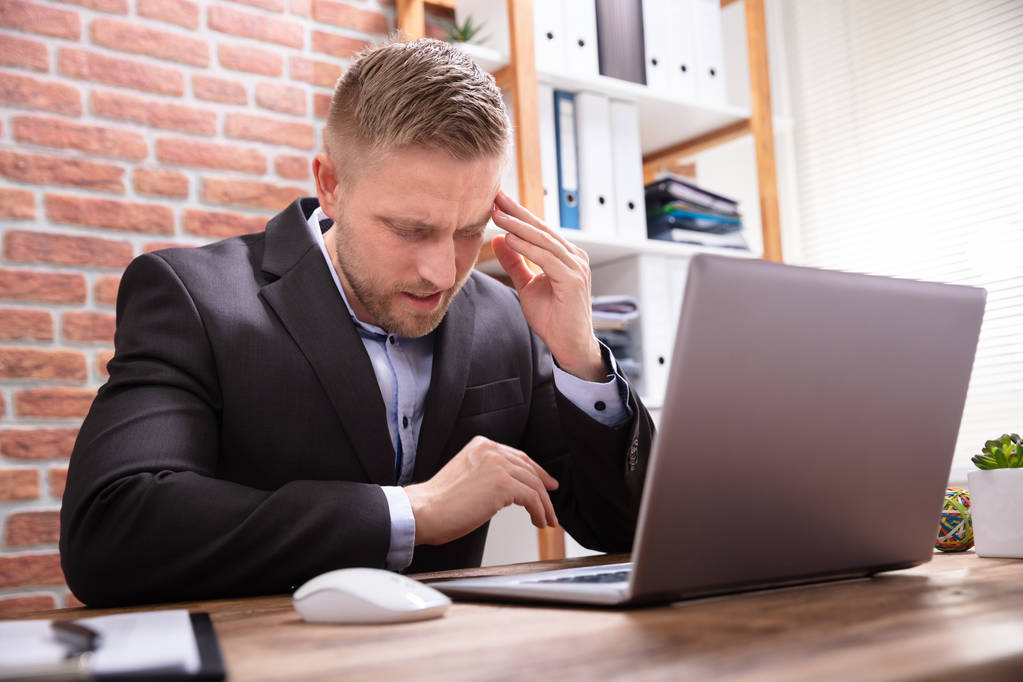 Jonge man lijdt aan hoofdpijn werken in het kantoor - Foto, afbeelding