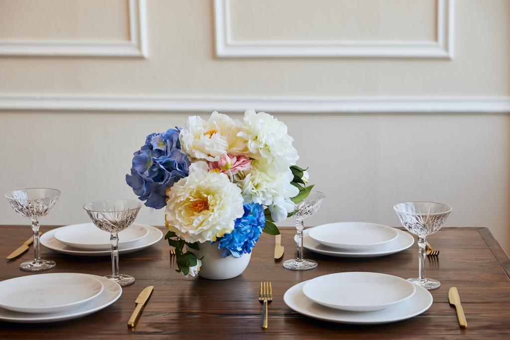 platos, cuchillos y tenedores, vasos de cristal y ramo en jarrón blanco sobre mesa de madera en restaurante
 - Foto, Imagen