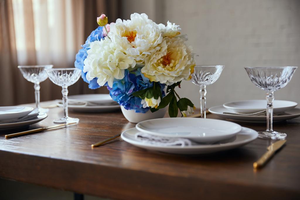 белые тарелки, хрустальные бокалы и цветы на деревянном столе дома
 - Фото, изображение