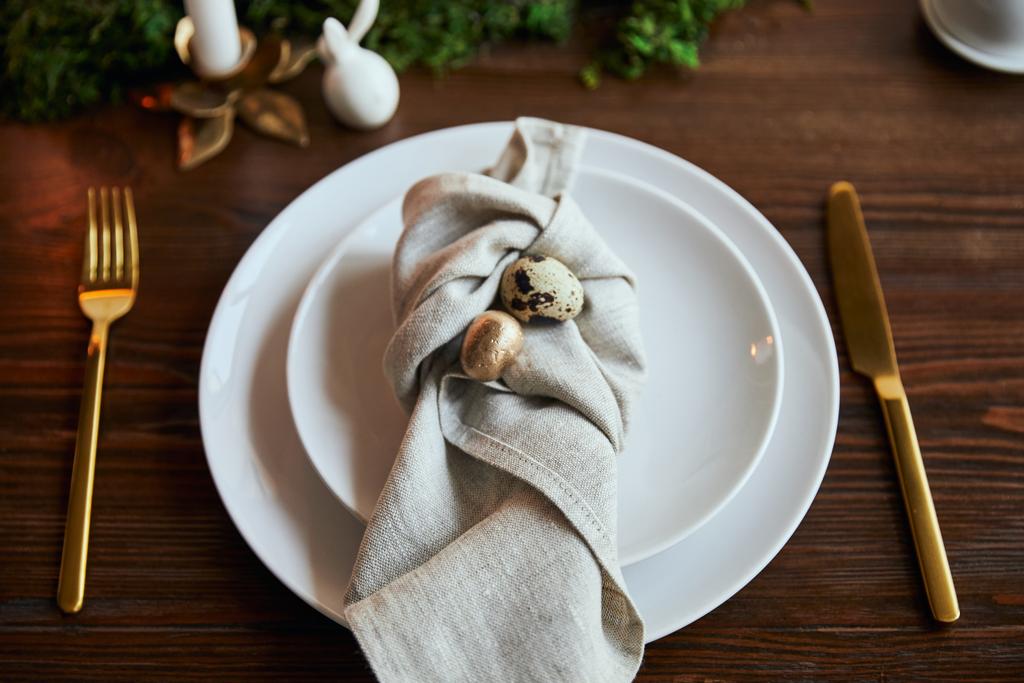 fuoco selettivo di uova di quaglia su tovagliolo e piatti vicino a muschio verde e posate su tavolo di legno
 - Foto, immagini