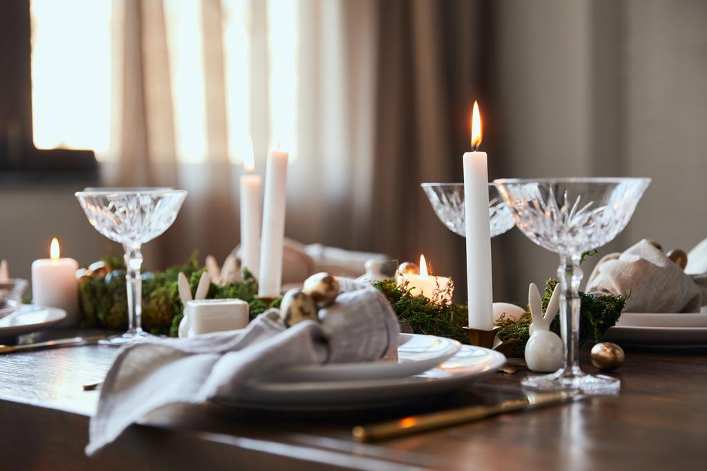 επιλεκτική εστίαση του αναμμένα κεριά κοντά σε πλάκες και κρυστάλλινα ποτήρια στο ξύλινο τραπέζι στο σπίτι - Φωτογραφία, εικόνα