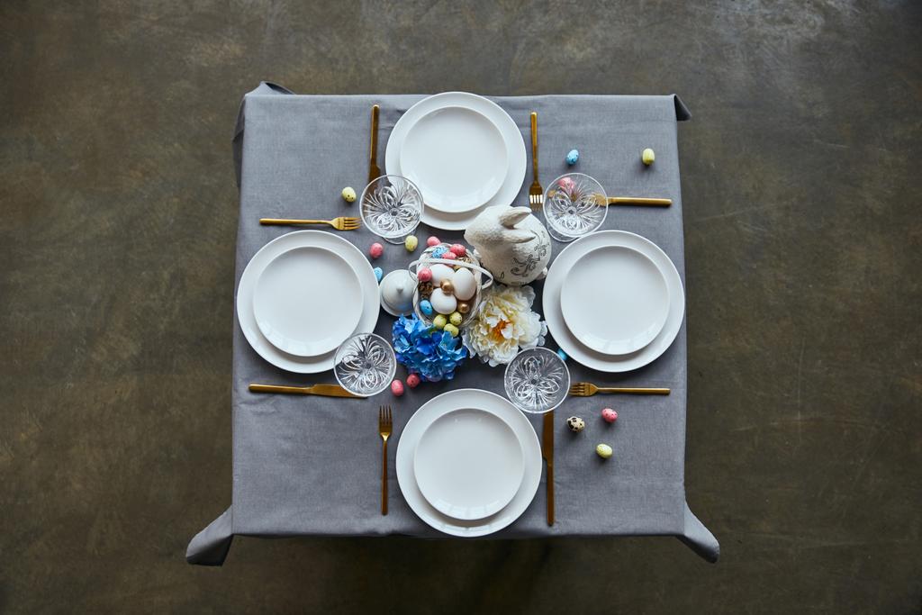 top view of table with white plates, cutlery, crystal glasses, cutlery, painted eggs and flowers at home - Photo, Image