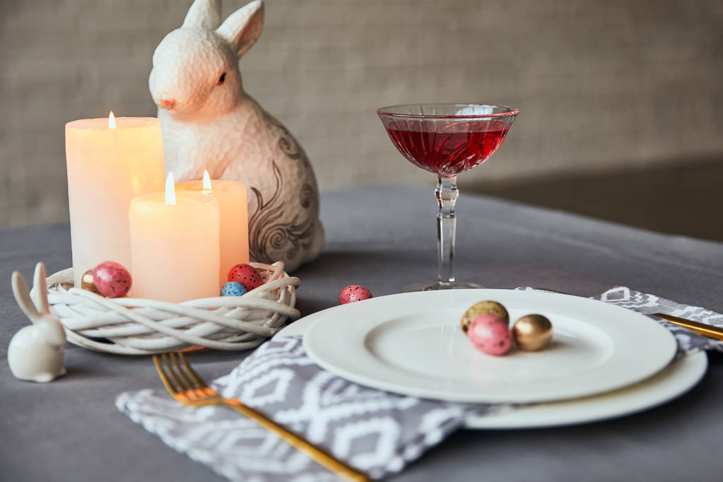 Selektywny fokus płyt z serwetka, jaja i świece w kosz, wino w szkła kryształowego i dekoracyjne królik na stole w domu - Zdjęcie, obraz