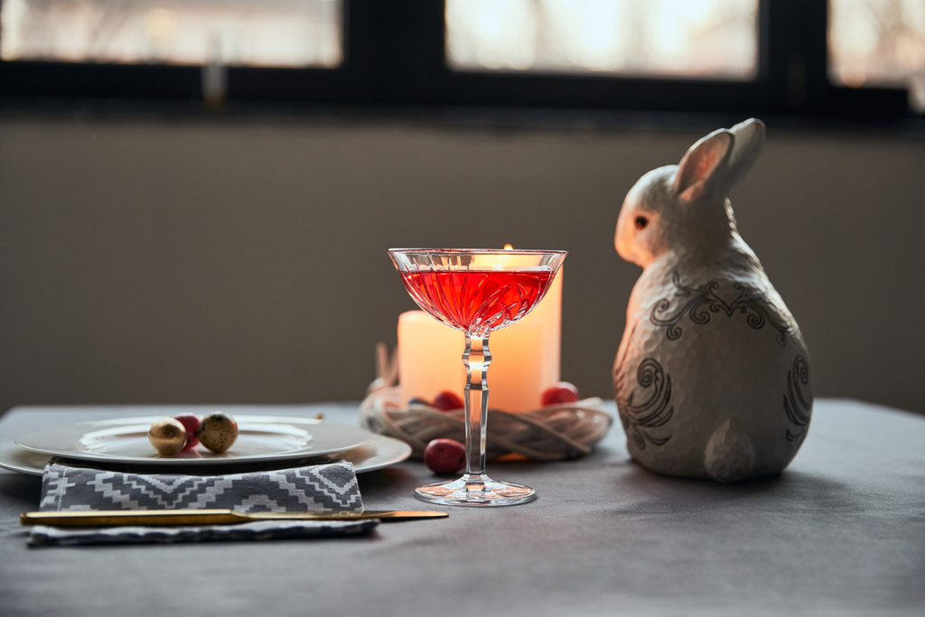 селективный фокус декоративного кролика, тарелки с яйцами, вино в хрустальном бокале, свечи на столе дома
 - Фото, изображение