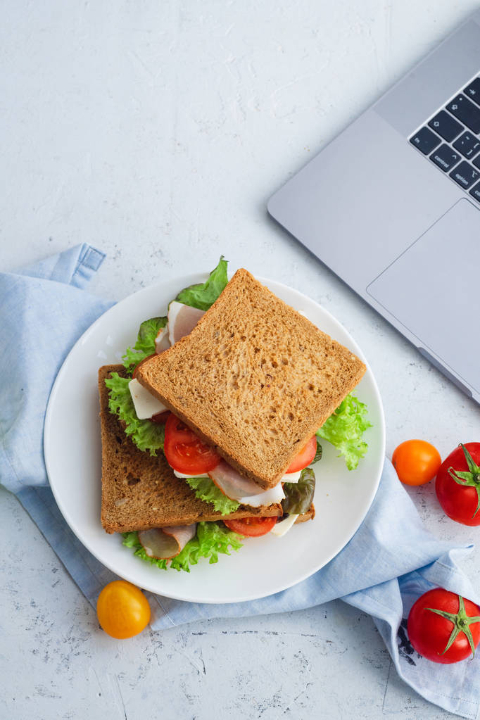sandwich sain avec légumes verts et jambon aux tomates et fromage dans une assiette près d'un ordinateur portable, idées de déjeuner pour le travail
 - Photo, image