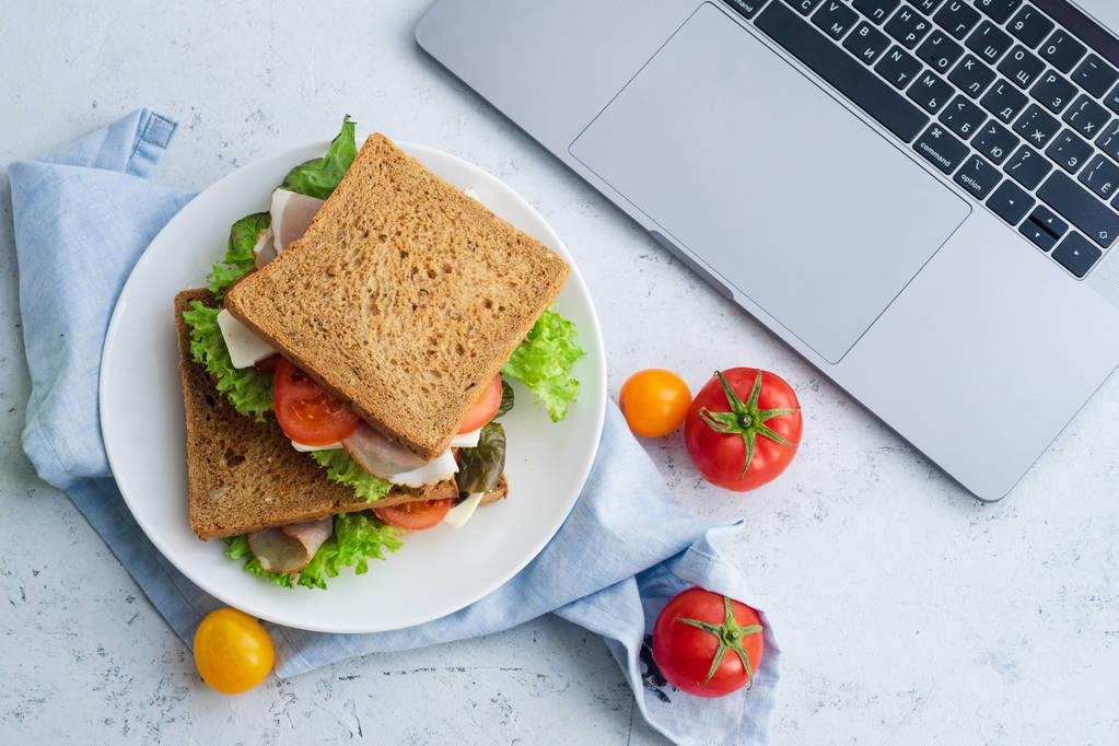sándwich saludable con verduras y jamón con tomates y queso en el plato cerca de la computadora portátil, ideas de almuerzo para el trabajo
 - Foto, Imagen