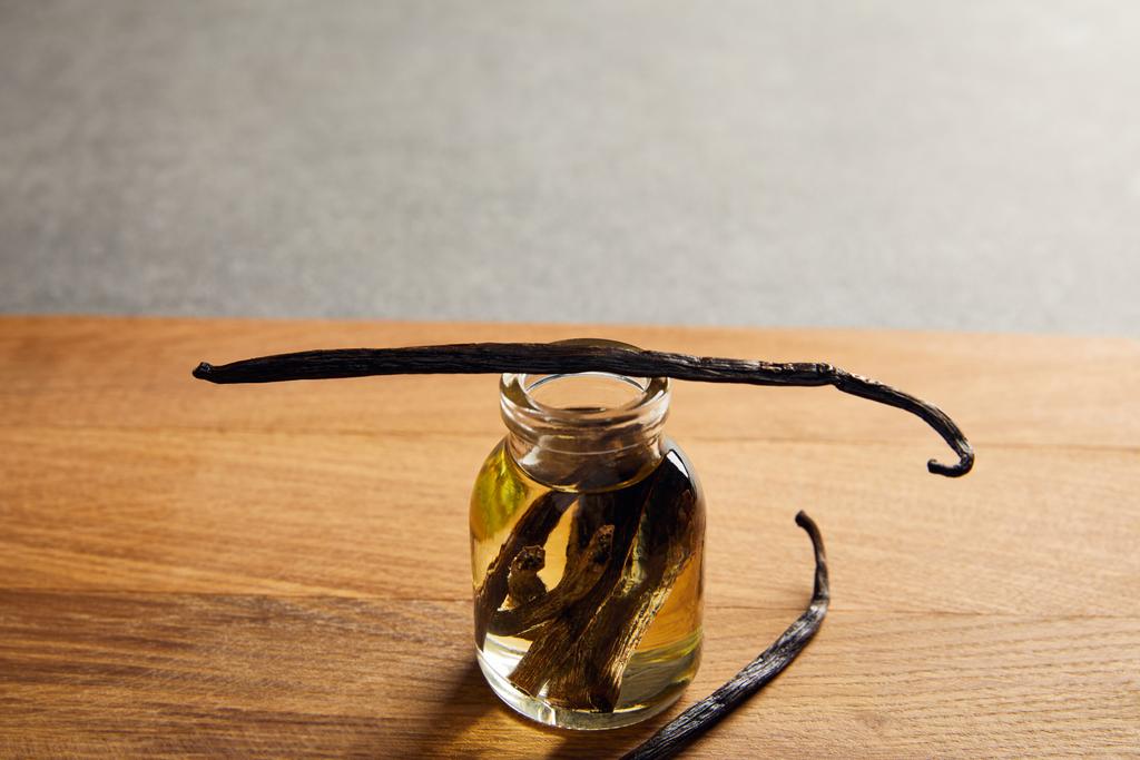 Flasche ätherisches Öl mit Vanilleschoten auf Holzoberfläche - Foto, Bild