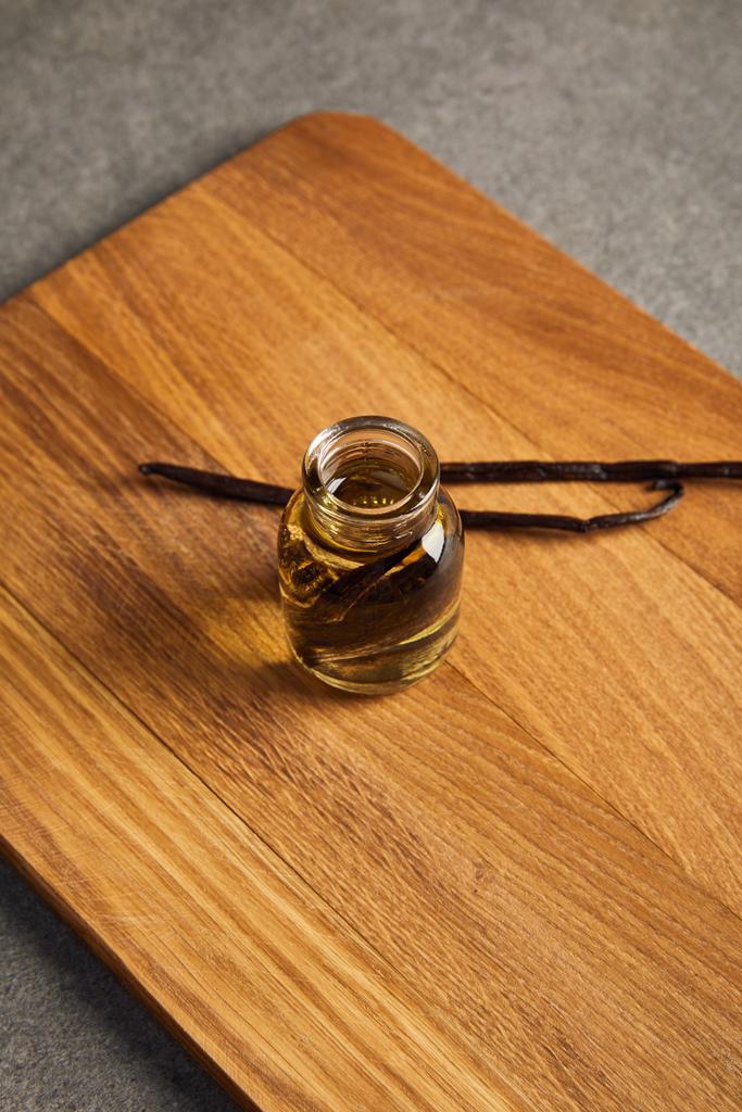 Botella de vidrio de aceite esencial con vainas de vainilla en tabla de cortar de madera
 - Foto, Imagen