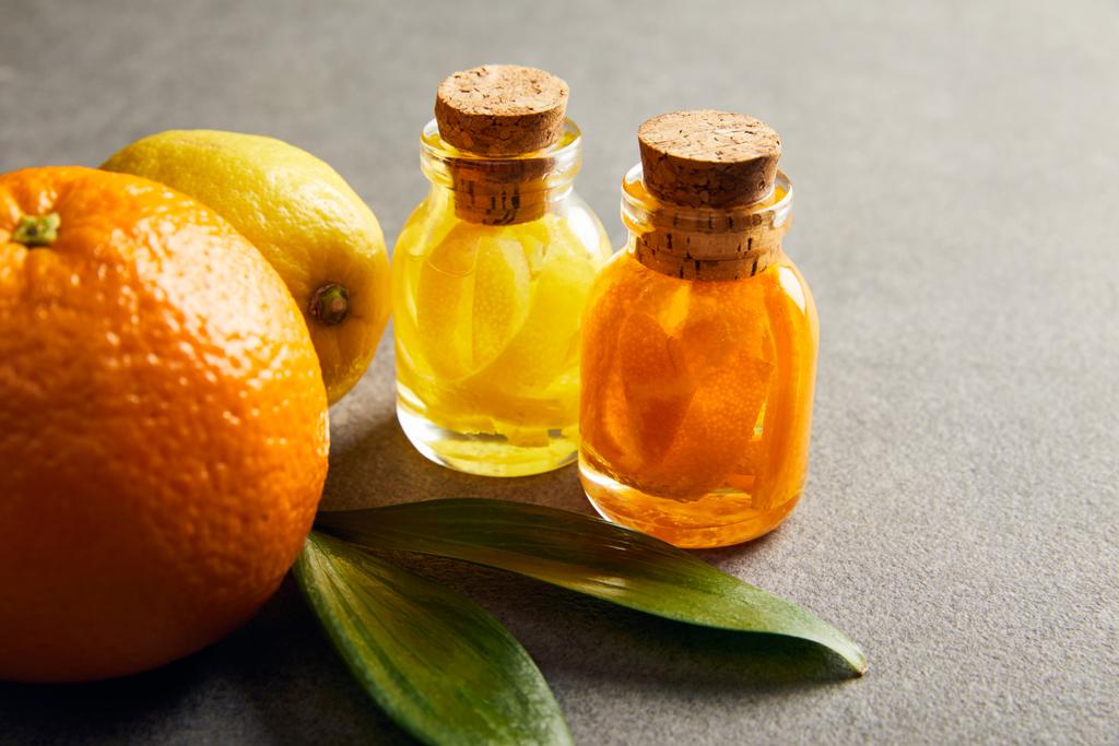 Glazen flessen van etherische olie met sinaasappel en citroen op donkere ondergrond - Foto, afbeelding