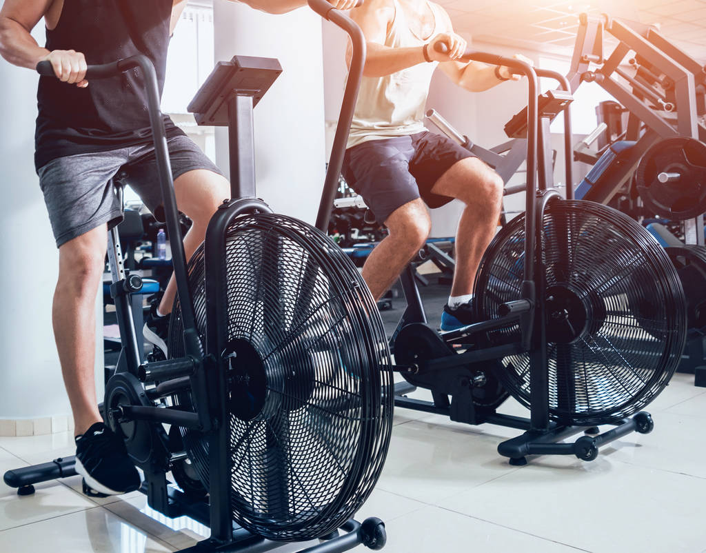 Hombres jóvenes con cuerpo muscular que utilizan la bicicleta neumática para el entrenamiento cardiovascular en el gimnasio de entrenamiento cruzado. Concepto Fitness
. - Foto, imagen
