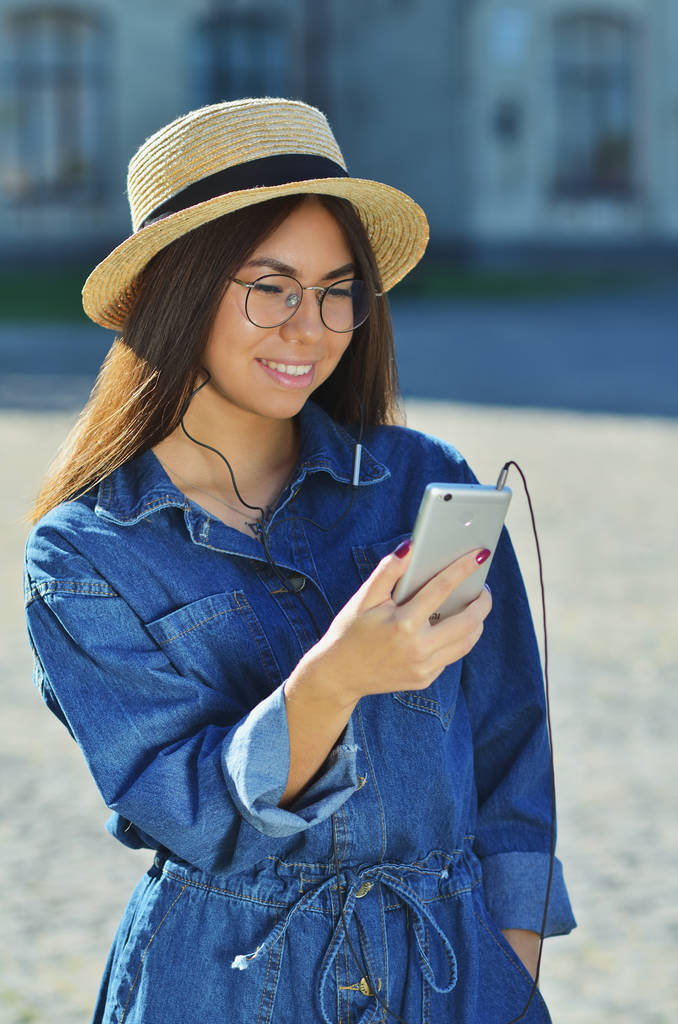 mladá asijská žena nosí sluneční brýle a džínové barvy stojící mimo s telefonem - Fotografie, Obrázek