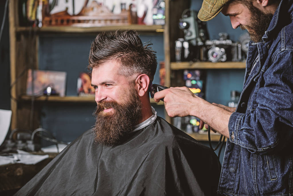 Borbély vágó hajjal az ügyfél tarkóján. A fodrász hajvágóval a szakállas fickó fodrászati hátterén dolgozik. Hipster ügyfél hajvágás. Hipster frizura koncepció - Fotó, kép