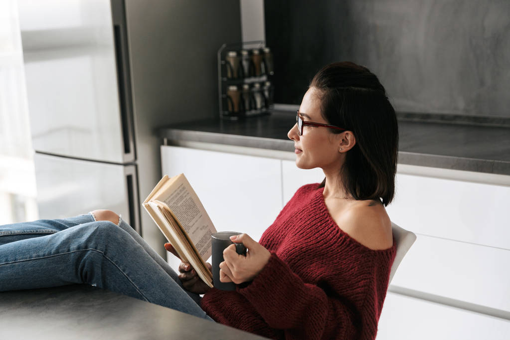 Красива жінка в приміщенні вдома на кухні читає книгу
. - Фото, зображення