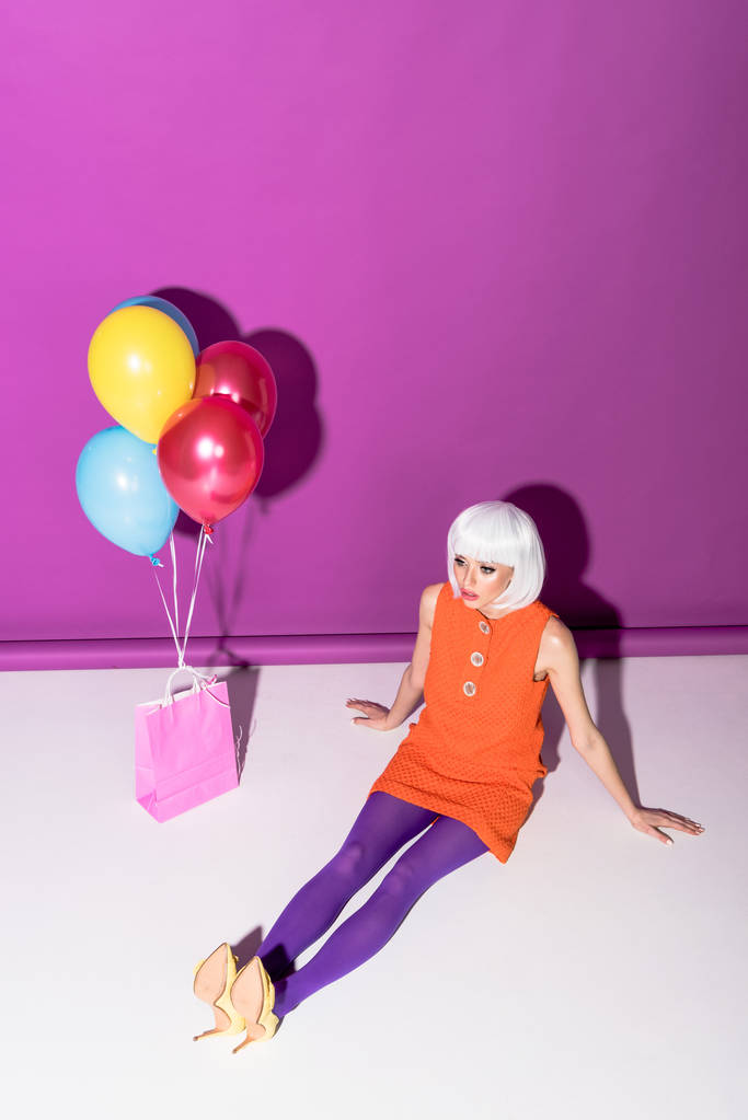 Superbe fille en perruque blanche avec des ballons à air assis sur fond violet
 - Photo, image
