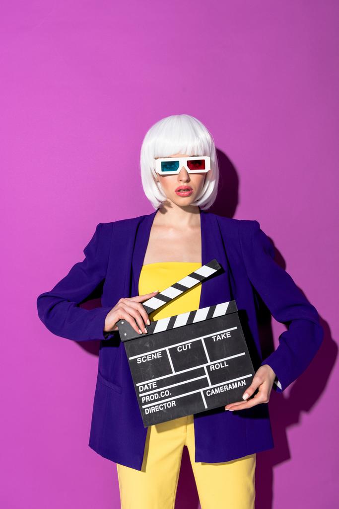 Young woman in 3d glasses holding clapperboard on purple background - Photo, Image