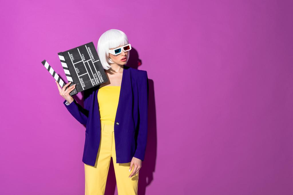 Femme élégante dans des lunettes 3D tenant clapperboard et regardant loin sur fond violet
 - Photo, image