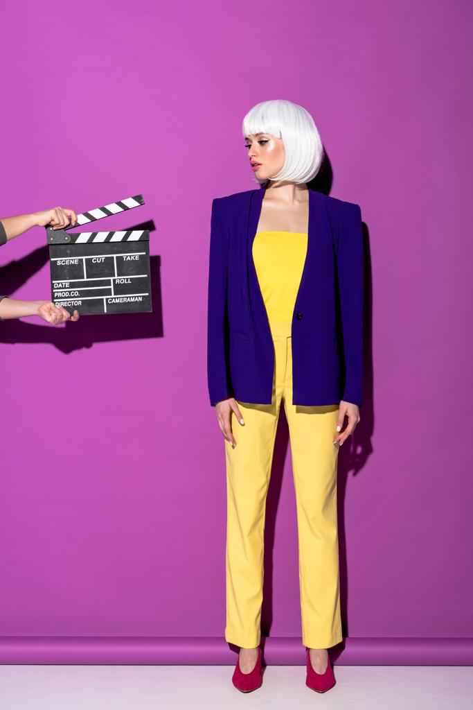Полный вид молодой женщины в белом парике, стоящей на фиолетовом фоне
 - Фото, изображение