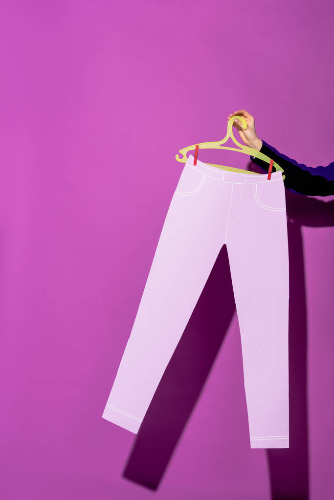 紫色の背景に紙パンツとハンガーを保持している女性のビューをトリミング - 写真・画像