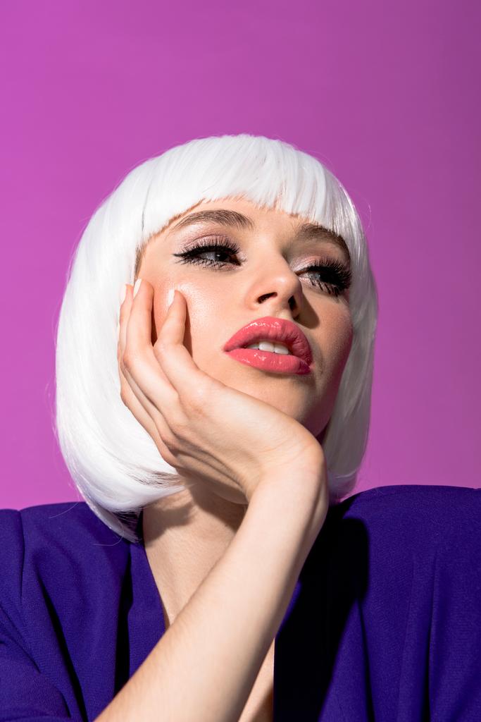 Богатая девушка с модным макияжем, поддерживающая лицо с изолированной рукой на фиолетовом
 - Фото, изображение