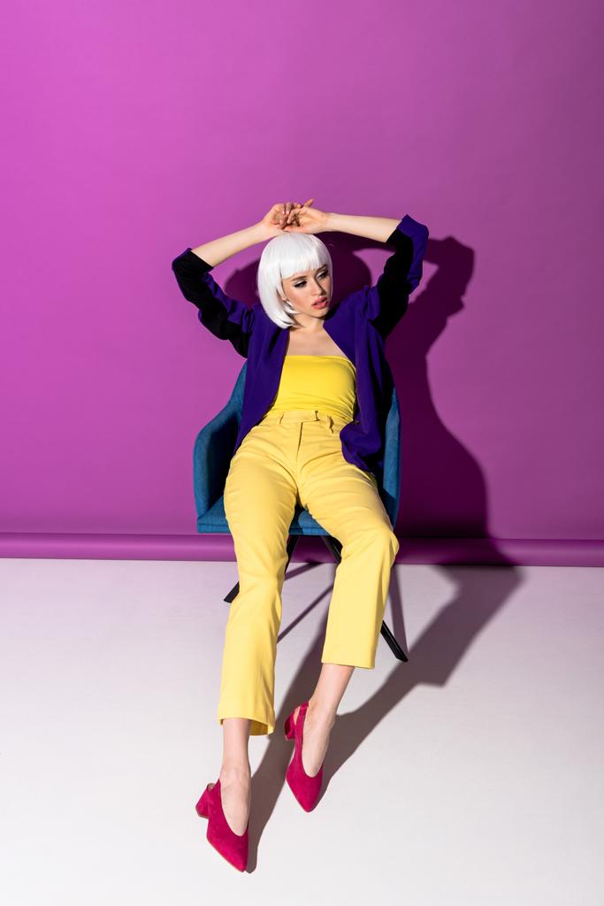 Preciosa joven en peluca blanca posando en sillón sobre fondo púrpura
 - Foto, imagen