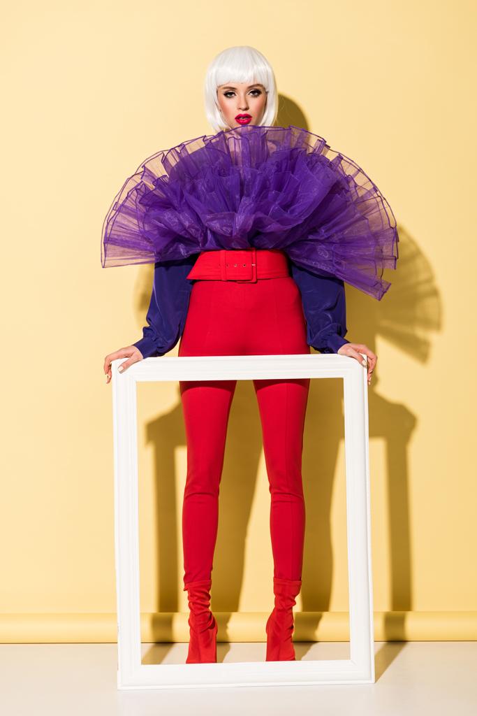 Full length view of woman in white wig holding frame on yellow background - Photo, Image