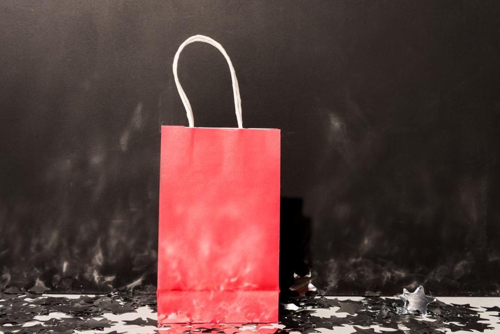 Красная сумка стоит на конфетти на темном фоне
 - Фото, изображение