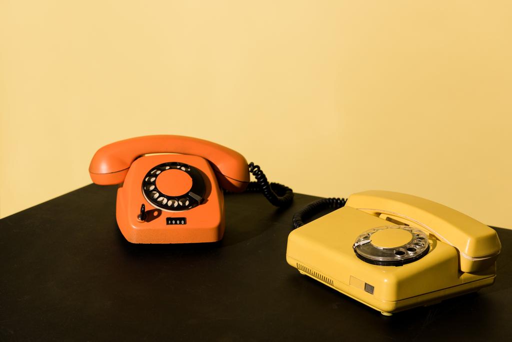 Dwa stare telefony na stół czarny na żółtym tle - Zdjęcie, obraz