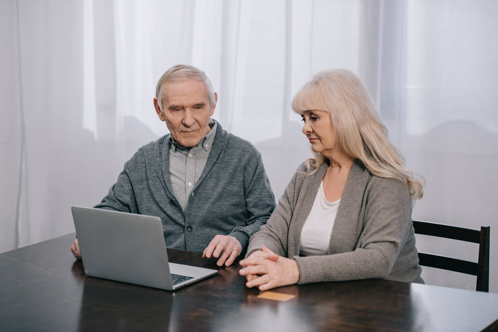 Verärgertes Senioren-Paar sitzt am Tisch und benutzt Laptop zu Hause - Foto, Bild