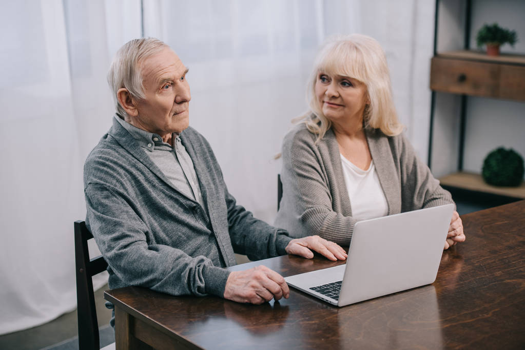 starší pár s šedými vlasy, sedí u stolu a použití přenosného počítače v domácnosti - Fotografie, Obrázek