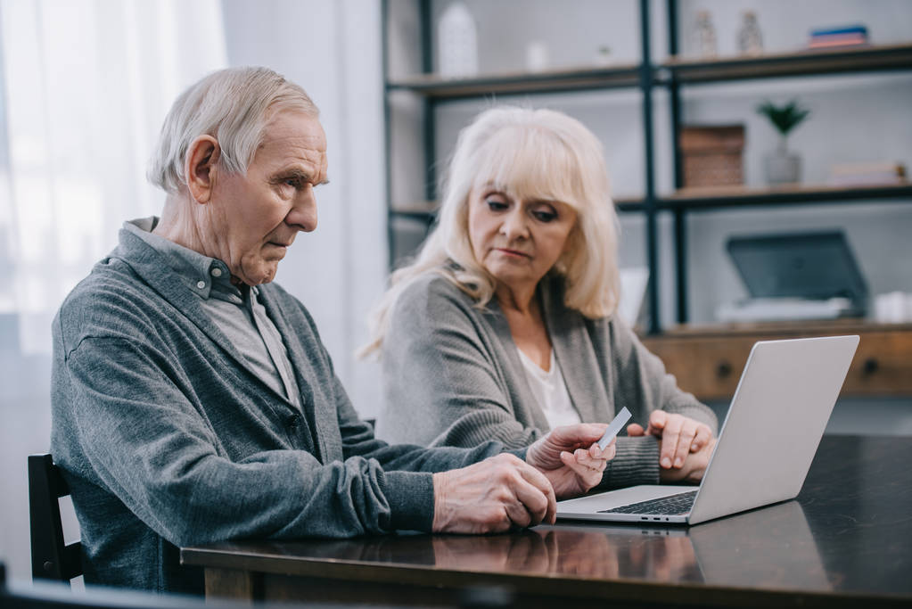 Seniorenpaar sitzt am Tisch und benutzt Laptop zu Hause - Foto, Bild