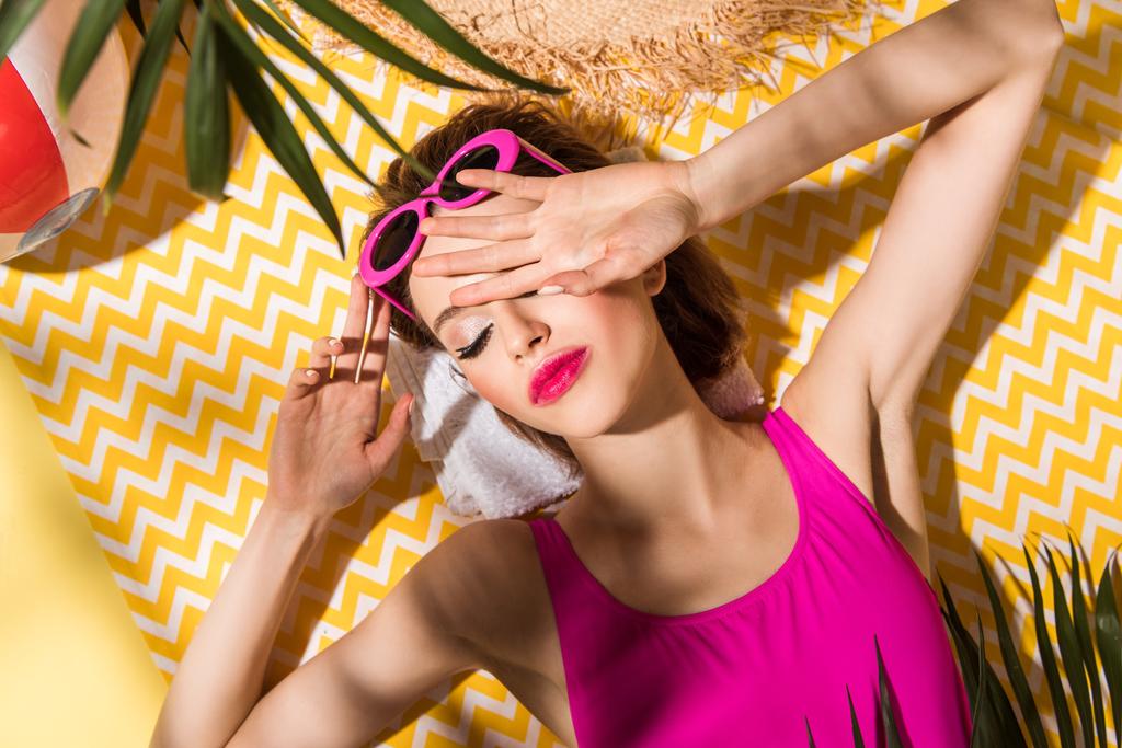 Вид сверху расслабленной женщины в солнцезащитных очках, лежащей с закрытыми глазами на поверхности.
 - Фото, изображение
