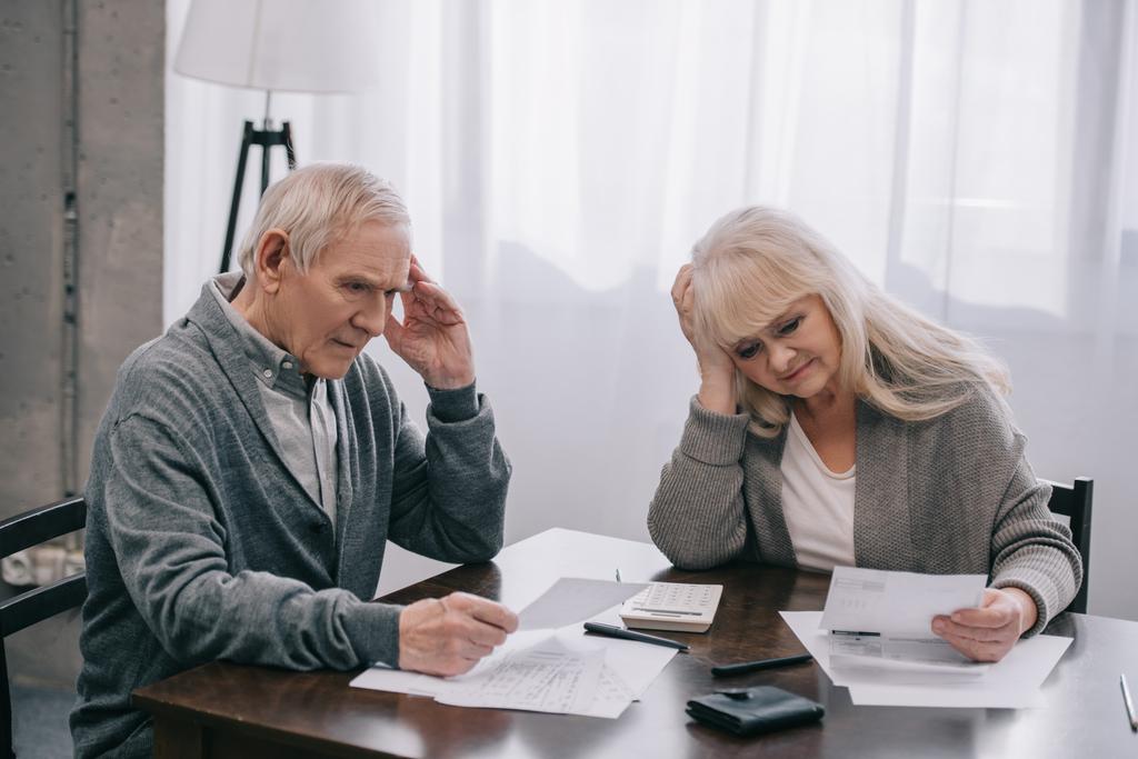 stressed senior couple with hands on head sitting at table and looking at bills  - Photo, Image