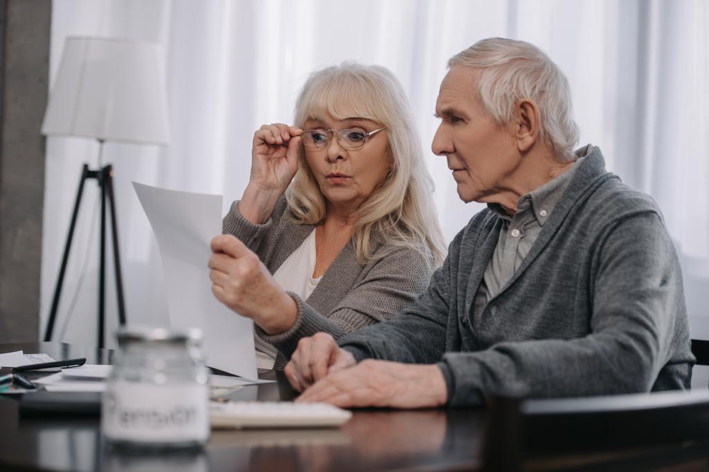 überraschtes Senioren-Paar sitzt am Tisch und schaut sich Rechnungen an  - Foto, Bild