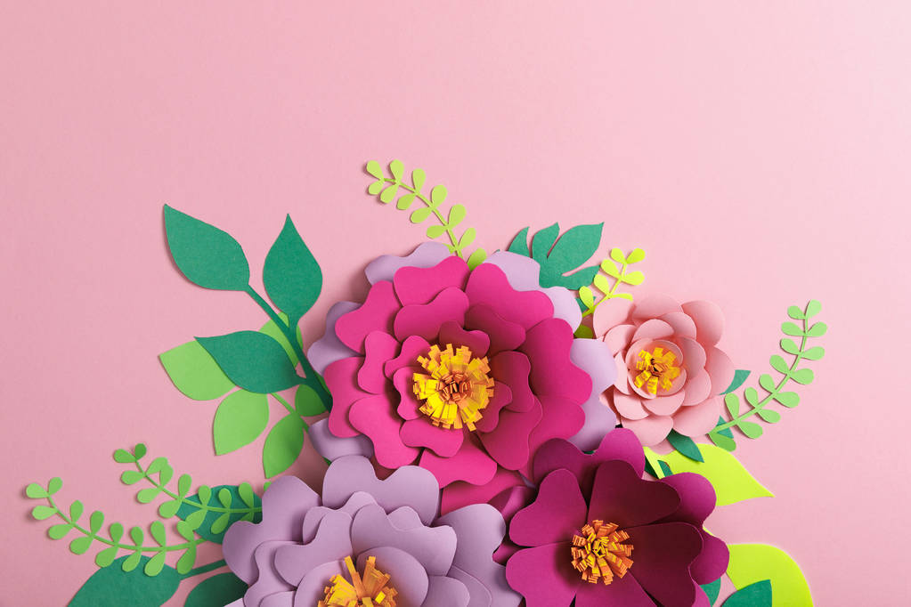 вид зверху на різнокольорові паперові квіти та зелене листя на рожевому фоні
  - Фото, зображення