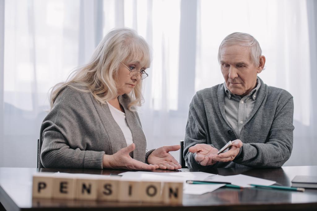 Senior para przy stole ze słowem 'pension' wykonane z drewnianych klocków na pierwszym planie - Zdjęcie, obraz