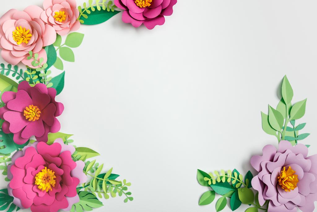 top view of multicolored paper flowers and green plants with leaves on grey background - Photo, Image