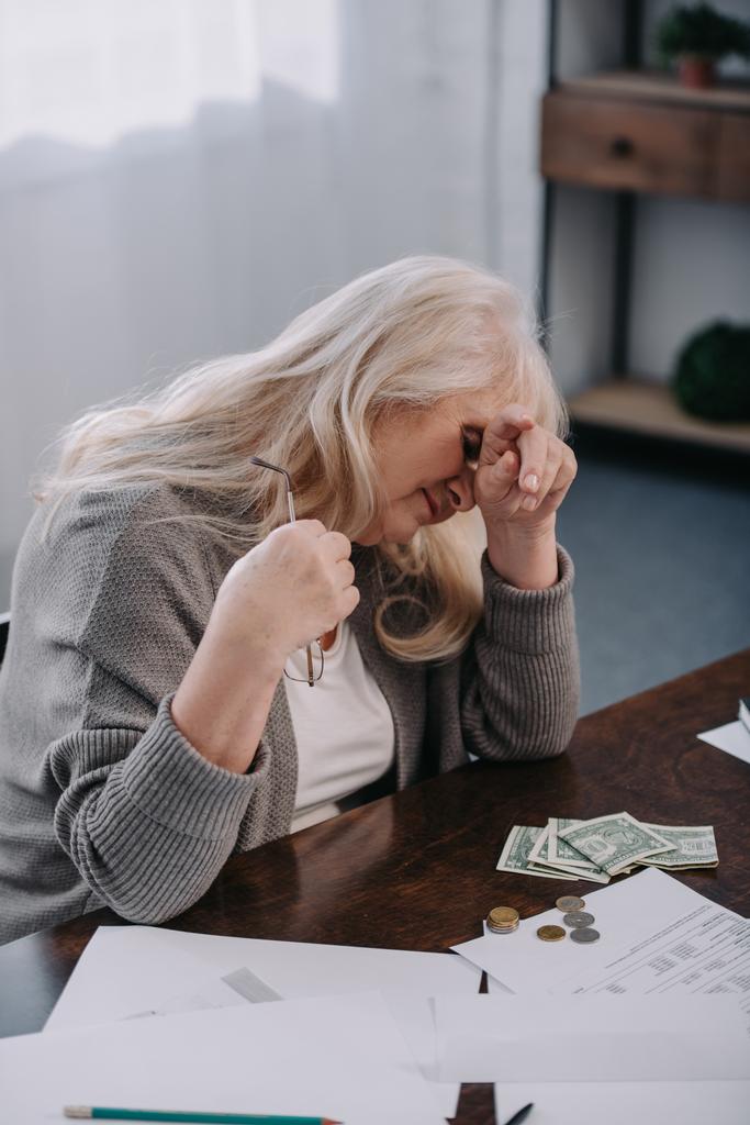 疲れている年配の女性のテーブルに座っていて、自宅でお金をカウントしながら頭痛 - 写真・画像