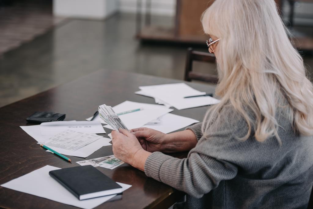 Seniorin sitzt mit Papierkram am Tisch und zählt Geld - Foto, Bild