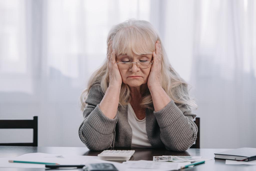 podkreślił starszy kobieta siedzi przy stole z pieniędzy i dokumentów podczas o ból głowy w domu - Zdjęcie, obraz