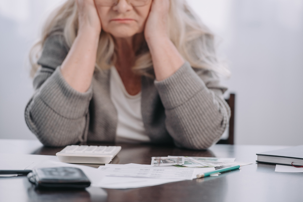 vista cortada da mulher idosa sentada à mesa com dinheiro e papelada, tendo dor de cabeça em casa
 - Foto, Imagem