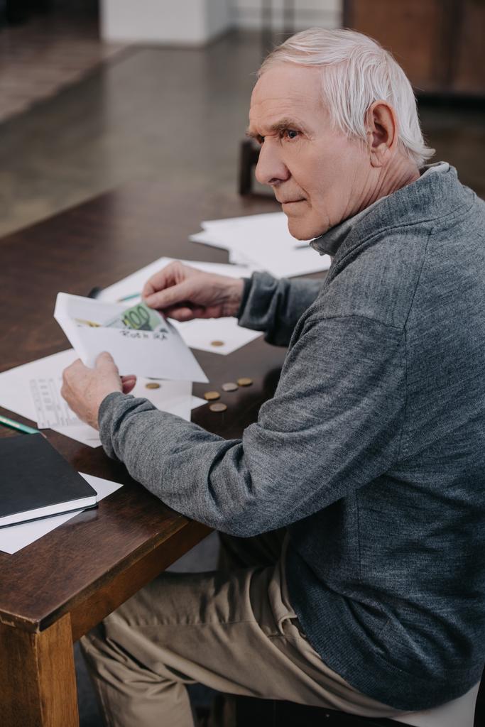 idősebb ember ül az asztal, a papírmunka és a gazdaság a borítékban pénz  - Fotó, kép