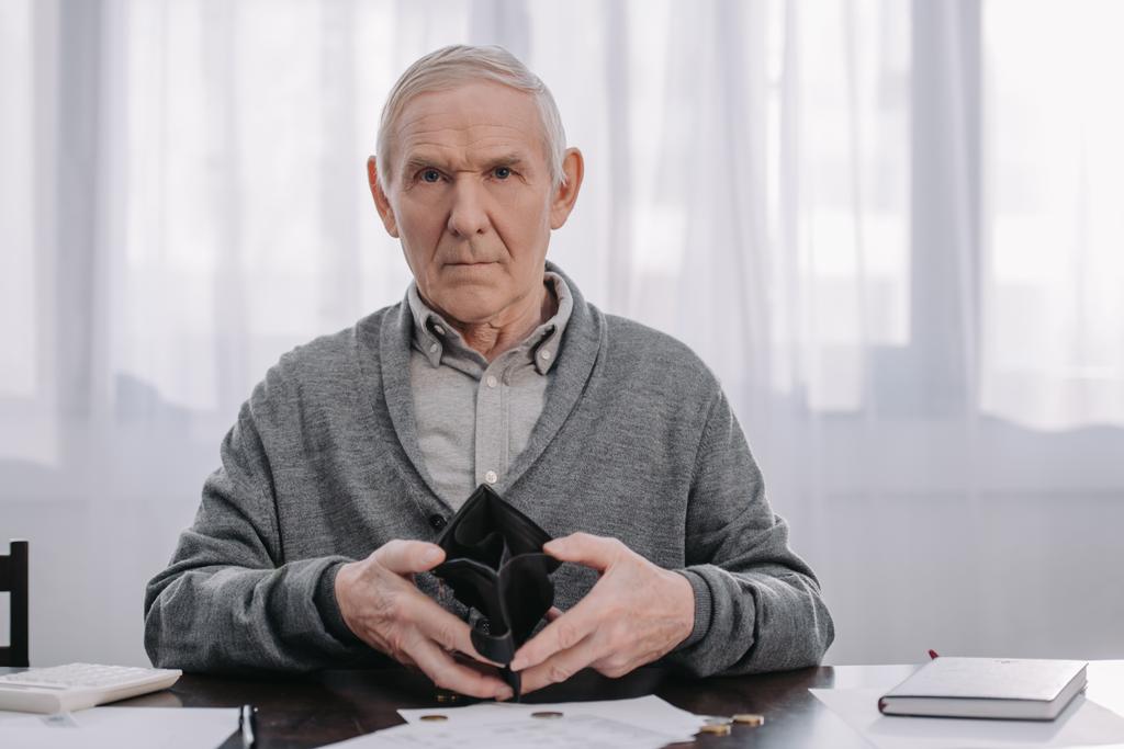 pensionato di sesso maschile seduto a tavola con scartoffie, guardando la macchina fotografica e tenendo il portafoglio vuoto
  - Foto, immagini