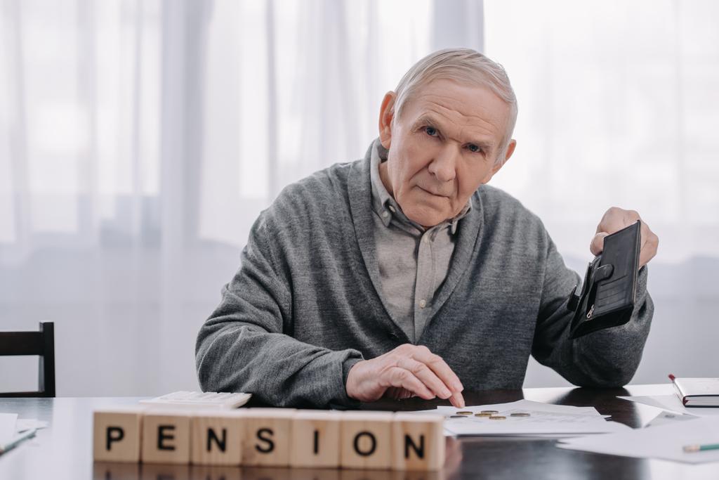 muž důchodce peněženku a papírování, sedí u stolu s slovo "důchodový" vyrobené z dřevěných bloků na popředí - Fotografie, Obrázek